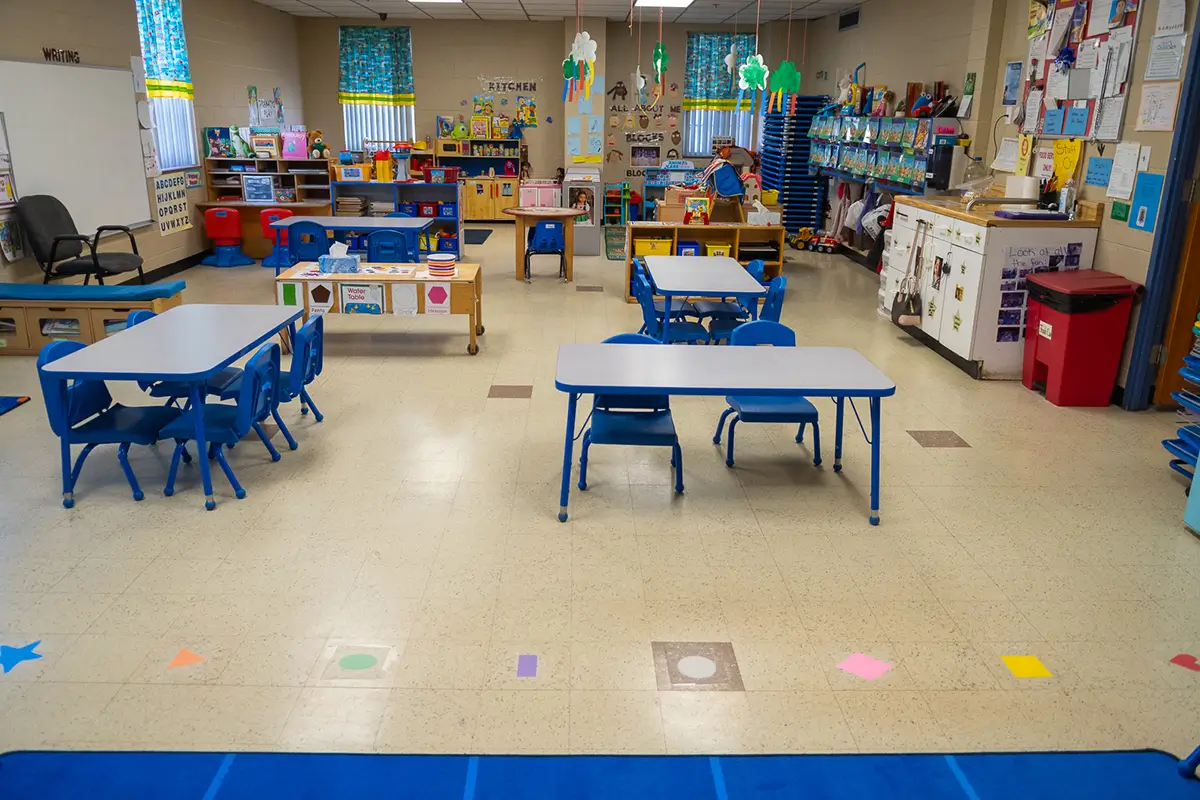 What Is a Child Care Center? - Child Care Inc Bright and organized child care classroom with small tables and chairs, learning stations, toys, and colorful decorations arranged for young children