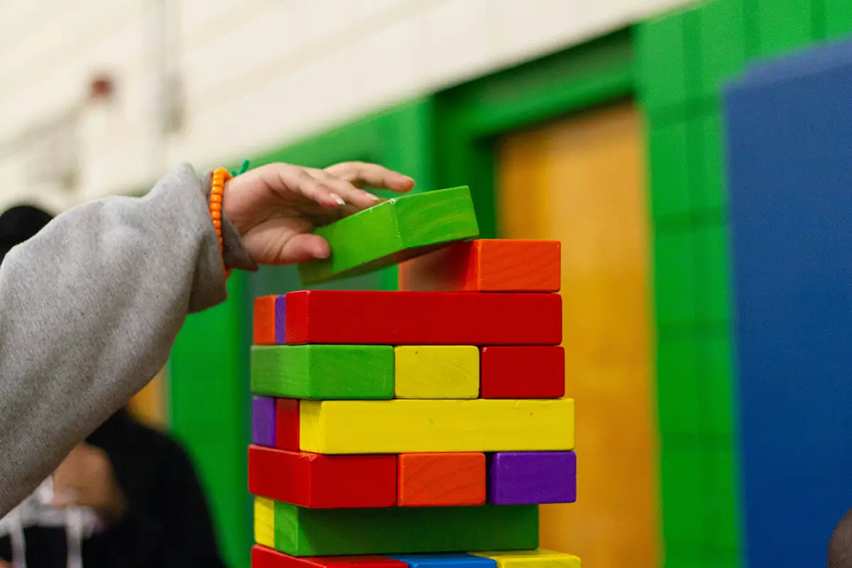 Questions to Ask During a Daycare Tour - Child Care Inc A close-up shot shows a child's hand carefully placing a bright green block onto a tall, colorful tower of wooden stacking blocks.