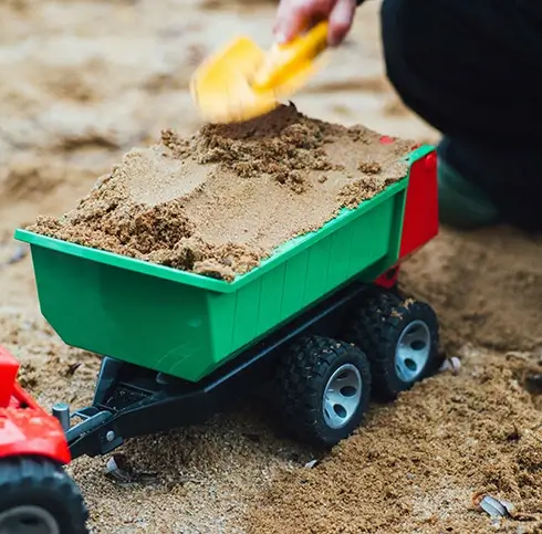 DHS-compatible A kid shoveling sand into a toy truck in a sandbox