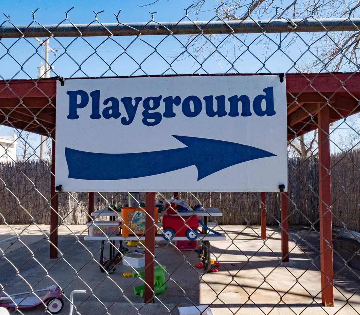 A sign attached to a chain link fence that says "Playground" with an arrow pointing right. 
